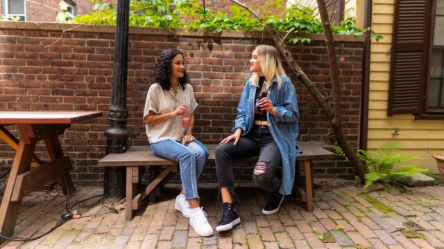 2 women sitting on brown wooden bench