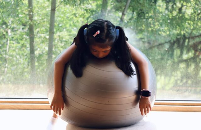 A woman sitting on top of a ball in front of a window