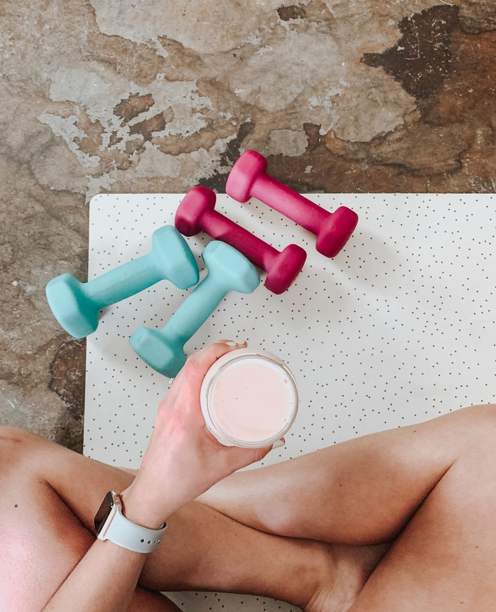Photo by Derick McKinney person holding white liquid filled cup above two pairs of dumbbells